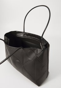 Zwarte schoudertas heeft een gladde, gemêleerde afwerking met een geometrisch patroon. Het heeft twee lange handvatten en een open bovenkant met een ruime binnenkant.