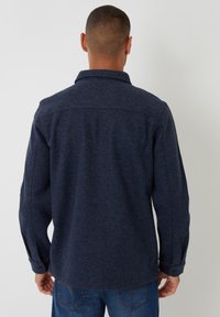 Marineblå uldskjorte med krave, knaplukning ved manchetterne og en let struktureret overflade, set fra ryggen. Tætsiddende design med synlige sømme.
