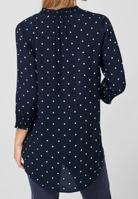 Donkerblauwe blouse met witte stippen, semi-doorzichtig materiaal, geplooide halslijn en driekwart mouwen met elastische manchetten; afgeronde zoom.