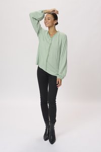 Blouse vert menthe avec des manches bouffantes et des détails froncés à l'avant, associé à un jean skinny noir et des bottines noires à bouts pointus.