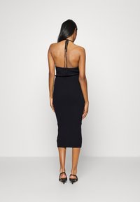 Vestido midi de malha canelada preta com design costas nuas e pescoço halter, apresentando uma silhueta justa e comprimento até aos tornozelos.