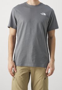 Harmaa lyhythihainen t-paita, joka on valmistettu puuvillasta. Siinä on pieni valkoinen logo rinnan kohdalla, klassinen pyöreä kaula-aukko ja sileä pinta.