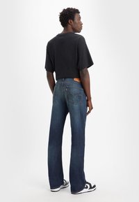 Zwarte cropped t-shirt, donkerblauwe spijkerbroek met een rechte pijp en achterzakken, sneakers met rubberen zool en zwart-witte accenten.