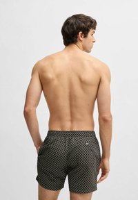 Pantaloni da bagno neri a motivo con design a diamante, vita elastica e tasche laterali, visti dal retro.