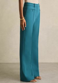 Teal levelekk trousers laget av glatt stoff, med skreddersydd midje, to frontlommer og presset brette detalj.