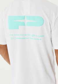 Camiseta de algodón blanca con letras gráficas grandes en color verde menta en la espalda, junto con texto impreso en un tono de menta más claro.
