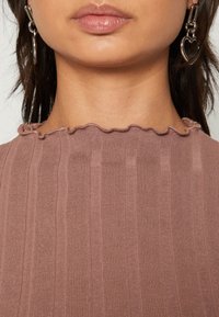 Ribbed, mauve top with a scalloped neckline, featuring vertical stripes and a soft texture. Silver heart-shaped earring visible.