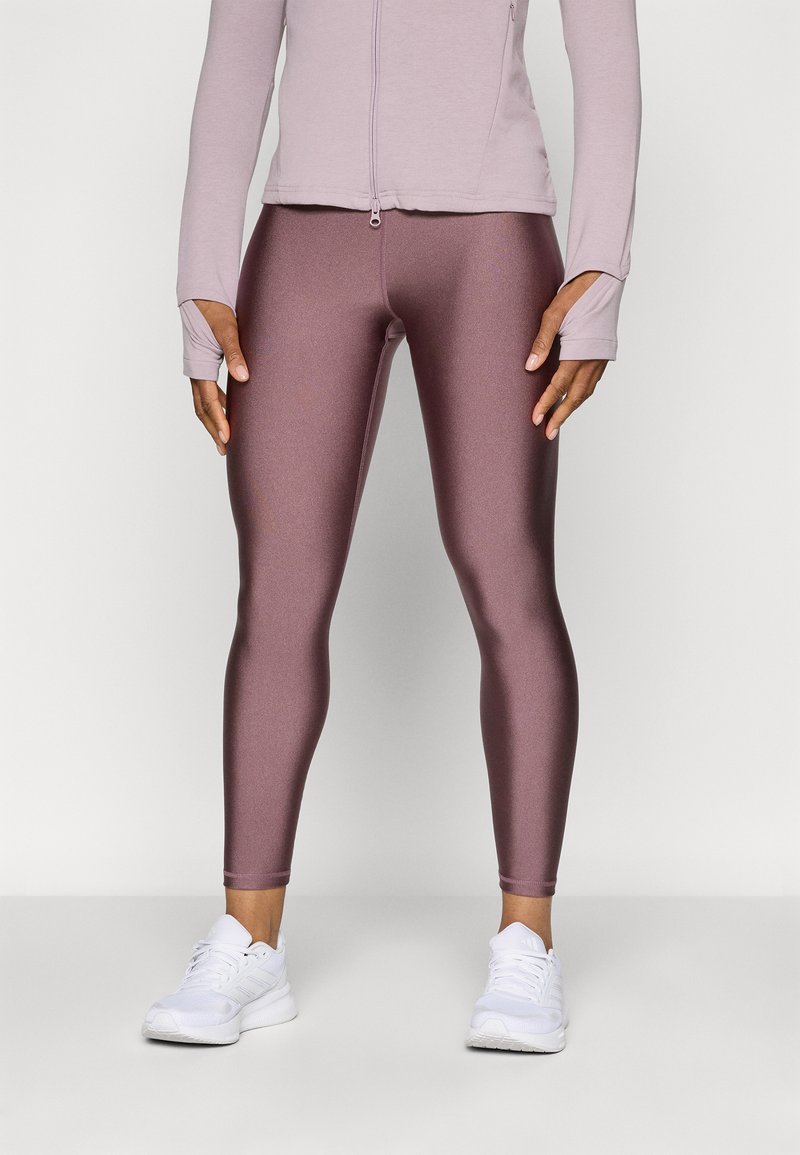 Bordeauxfarbene, metallische Leggings in schmaler Passform, kombiniert mit einer helllila Reißverschlussjacke. WeißeSportschuhe vervollständigen das Outfit.