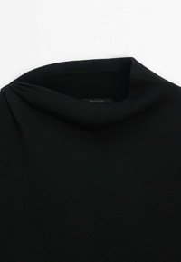 Pull en maille noire avec un col montant légèrement replié, montré de la poitrine supérieure jusqu'au col.