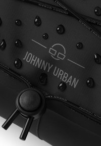 Czarna wodoodporna torba z materiału z wypukłymi kroplami, zamknięciem na zamek błyskawiczny oraz nadrukowanym tekstem „JOHNNY URBAN” z graficznym logo.