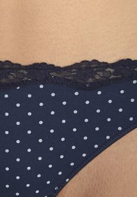 Marineblauwe bikini met stippen en zilveren stippen; kantafwerking langs de bovenkant. Gladde textuur met een aansluitend ontwerp en naadloze randen.