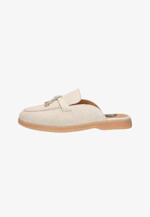 Beige suède instapper met een tan rubberen zool en een goudkleurige kettingdetail op het bovenwerk, ontworpen voor casual gebruik.