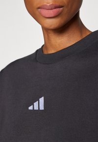 Črna bombažna sweatshirt s krojnim ovratnikom in belim vezenim logotipom s tremi naraščajočimi črtami na levi prsni strani.