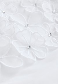 Tejido blanco con bordado floral, adornado con pétalos transparentes y acentos de cristal. La textura parece suave con un diseño delicado y en capas.