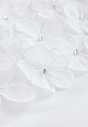 Teea albă cu broderie florală, având petale transparente și accente de cristale. Textura pare netedă, cu un design delicat, stratificat.