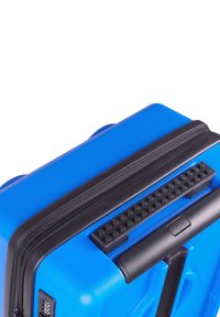 Blue hard-shell suitcase with a textured black zipper and handle. Features a combination lock and a patterned rubber grip on the handle.