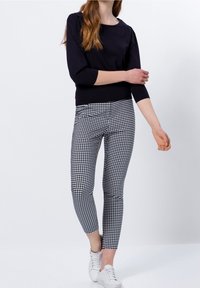 Zwarte driekwart mouwtrui gecombineerd met zwart-wit geruite leggings, met een slim-fit ontwerp en gladde stof. Witte sneakers maken de outfit af.