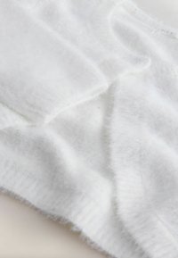 Weißer, flauschiger Strickstoff mit einer weichen, strukturierten Oberfläche. Verfügt über sanfte Falten und einen gerippten Saum, der Wärme und Komfort vermittelt.