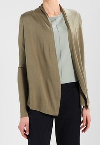 Olive zielony lekki kardigan z otwartym przodem, długimi rękawami i swobodnym krojem. Nałożony na jasnoniebieski dopasowany top.