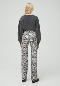 Pull court noir associé à un pantalon taille haute à jambes larges avec un motif zébré noir et blanc, souligné par une ceinture à la taille.