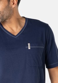 T-shirt bleu marine à col en V avec manches courtes, doté d'une poche sur la poitrine gauche et de coutures contrastées. Confectionné en coton doux.