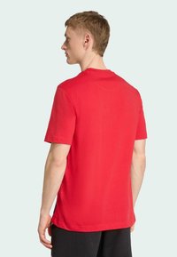Camiseta roja de manga corta hecha de algodón, con un escote redondo y una textura suave. La vista trasera muestra las costuras de los hombros y un dobladillo recto.