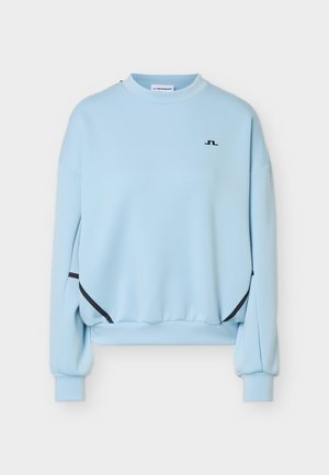 Sweat-shirt bleu clair à manches longues avec col rond, accents noirs incurvés près des côtés inférieurs et petit logo noir sur le haut gauche de la poitrine.