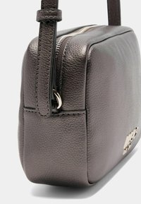 Læder crossbody taske i mørkegrå; rektangulær form med tekstureret overflade. Har en sølvfarvet lynlås og et metallisk logo-accent.