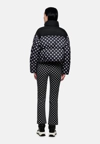 Daunenjacke mit schwarzem Oberteil und unterem Teil im Sternenmuster, kombiniert mit schwarz-weißen gemusterten Hosen und passenden schwarzen Schuhen.