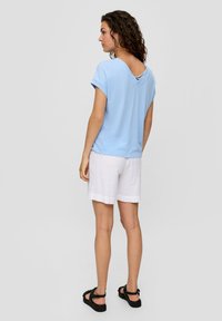 Lichtblauw kort mouwtop met een V-achterkant ontwerp, gecombineerd met witte shorts. De stof lijkt zacht, met een casual pasvorm en opgerolde mouwen.