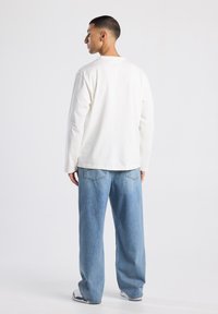Langarm, ronde hals witte shirt gecombineerd met lichtblauwe, loszittende denim jeans, met achterzakken en een ontspannen pasvorm.