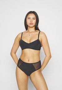 Black bikini featuring a smooth, matte texture; the top has a v-neck design with thin straps, and the high-waisted bottom includes sheer sections.