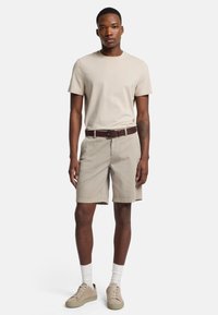 Beige katoenen T-shirt, beige shorts met een riem, gecombineerd met beige sneakers en witte sokken. Eenvoudig ontwerp, zonder patronen of logo's.