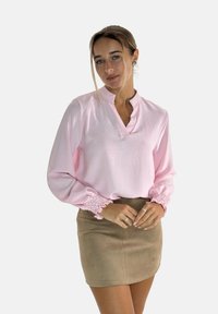Blusa rosa chiaro a maniche lunghe con una mezza abbottonatura e polsini arricciati, abbinata a una minigonna in camoscio beige. Tessuto liscio, vestibilità sartoriale.