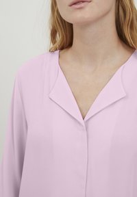 Blusa rosa chiaro con colletto a punte, chiusura a bottoni e texture liscia, dal fit rilassato e maniche lunghe.