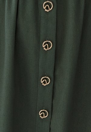 Tejido verde oscuro con seis botones dorados redondos de diseño retorcido, dispuestos verticalmente en la parte frontal. Textura suave con un brillo mínimo.