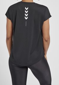 Black athletic top with short sleeves, featuring a reflective chevron pattern on the back. Soft, lightweight fabric with a relaxed fit.