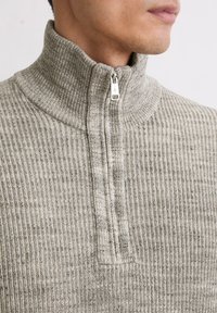 Fleece-Half-Zip-Pullover in Hellgrau mit gerippter Textur. Verfügt über einen hohen Kragen und einen silbernen Reißverschluss. Glattes Material mit dezentem Muster.