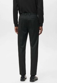 Pantaloni negri personalizați cu o textură netedă, având o croială regulară, talie elastică și buzunare la spate. Purtați cu pantofi negri de dress.