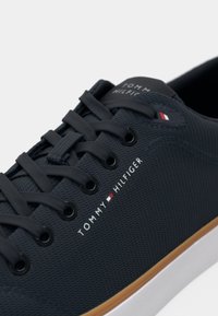 Marineblå Tommy Hilfiger sneaker med tekstureret overdel, sorte snørebånd, hvid logo tekst, lille rød-hvid-blå flag og hvid sål med brunt trim.