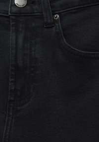 Jean en denim noir à la texture lisse, avec une poche avant, des coutures apparentes et un bouton métallique gravé "Depuis 1991".