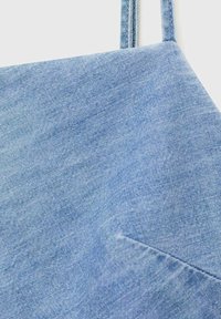 Tissu en denim bleu clair avec une texture lisse, présentant des coutures diagonales et de fines bretelles réglables. Le matériau semble doux et respirant.