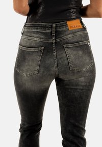 Jeans de mezclilla lavados en negro con un corte ajustado, que cuentan con un parche de cuero en la cintura y bolsillos con un acento en forma de corazón.