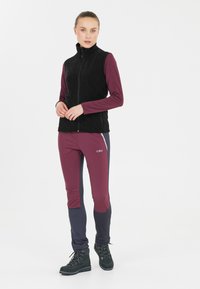 Sort fleece vest med høj krave, parret med en langærmet maroon top og tætsiddende bukser med maroon og navy sektioner. Sorte støvler inkluderet.
