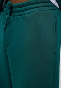 Teal joggings gemaakt van zachte stof, met een elastische tailleband met trekkoord en een zijzak. Soepele textuur en getailleerde pasvorm.