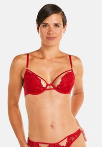 Soutien-gorge en dentelle rouge avec des motifs floraux délicats, des bretelles réglables et un design strappy unique. Fini lisse avec des accents matériels minimaux.