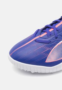 Fioletowe syntetyczne sneakersy z różowymi akcentami i teksturowaną powierzchnią. Posiadają białą gumową podeszwę i wzorzysty detal po bokach.