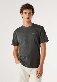 Grijze katoenen t-shirt met korte mouwen en een ronde hals, voorzien van een klein wit logo op de linkerkant van de borst. Soepele textuur.