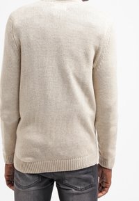 Beżowy sweter dzianinowy z teksturowaną powierzchnią, prążkowanymi mankietami i dołem. Posiada okrągły dekolt i luźny krój.