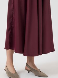Abito di satin bordeaux con un design fluido e un orlo elegante. Scarpe slingback in camoscio grigio con tacco basso e dettaglio a punta.